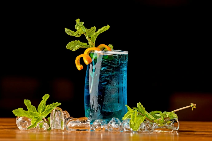 a tall glass filled with blue liquid and garnished with orange slices